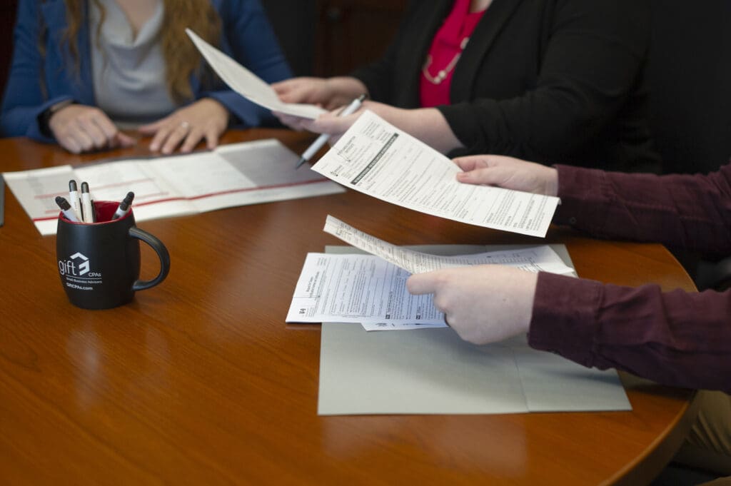 Three people sit at a desk, looking over paperwork.